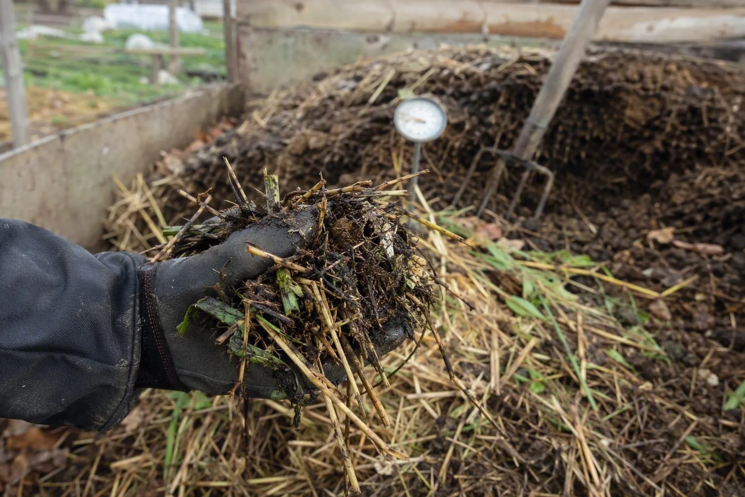 A hand lifts leafy greens, straw, and twigs from compost, showing the coarse spaces that help the heap breathe.